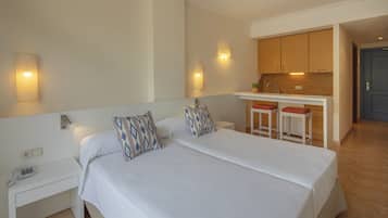 Habitación de hotel con cama doble, mesitas de noche, un escritorio pequeño con teléfono, una kitchenette con taburetes y una puerta que da a otra habitación.
