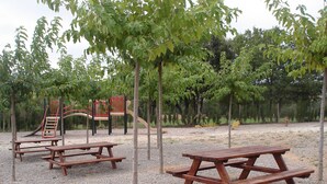 Un parque infantil con toboganes y columpios, rodeado de árboles y mesas de picnic.