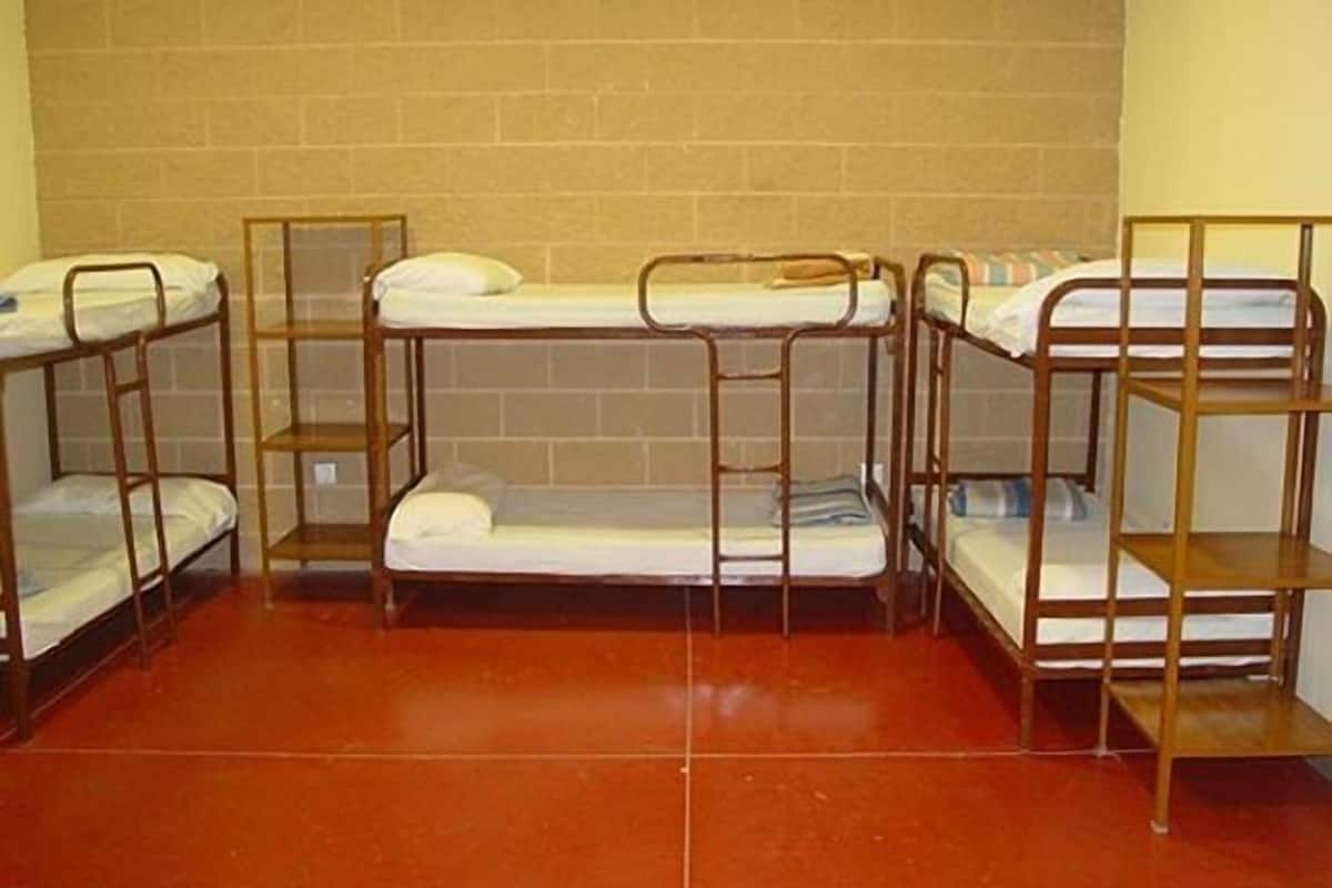A dormitory room with four bunk beds, a tiled floor, and a brick wall.