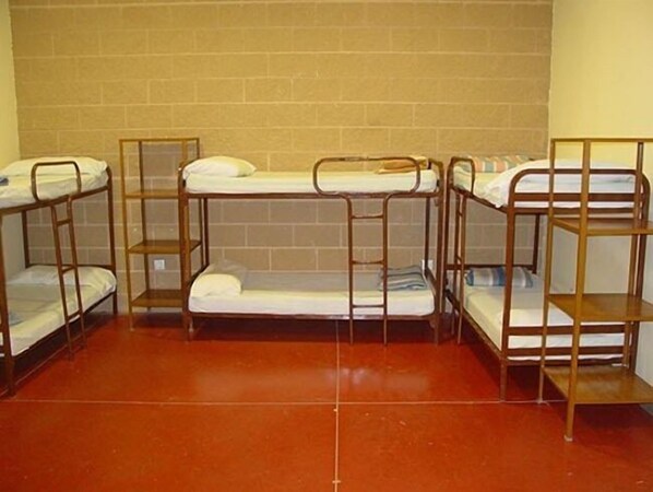 A dormitory room with four bunk beds, a tiled floor, and a brick wall.