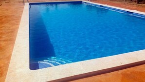 Una piscina rectangular con agua azul cristalina, rodeada por una terraza de tonos claros.