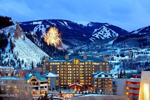 A hotel with multiple floors, a prominent entrance, and a view of snow-covered mountains. - Charlie Rentz: Remodeled, Wraparound Deck, Gondola, Resort Amenities, Pool + Hot Tubs (Avon)