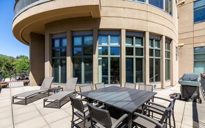 Une terrasse extérieure avec une table et des chaises, un barbecue et une vue sur un immeuble doté de grandes fenêtres.