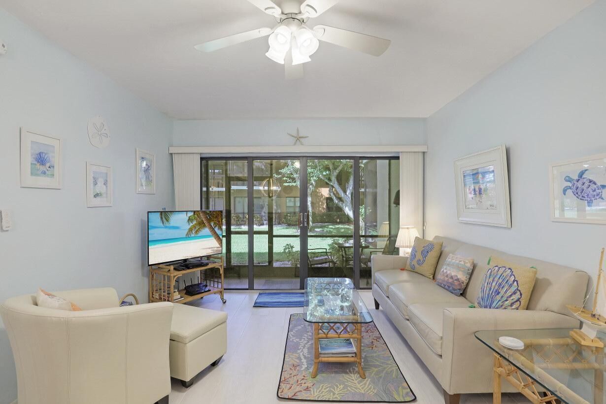 A living room with a sofa, a glass coffee table, a TV, and a ceiling fan.