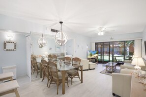 A spacious living area with a dining table, chairs, and a sofa. There is a television and a ceiling fan. - Relaxing Condo With two Pools and Steps to Beach (Marco Island)