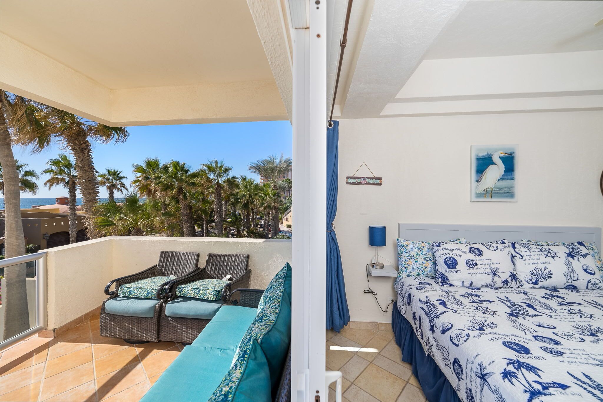 Un balcone con mobili in vimini e un letto con copripiumino a motivi blu e bianchi.