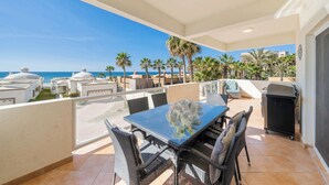 An outdoor patio with a table and chairs, overlooking a beach with palm trees and buildings in the background. - Las Palmas 2BR 2BA Suite 2nd FL Ocean View G205 (Puerto Peñasco)