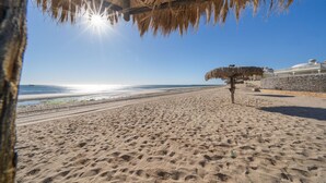 A beach with a thatched umbrella, clear sky, and a building in the background. - Las Palmas 2BR 2BA Suite 2nd FL Ocean View G205 (Puerto Peñasco)