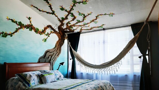 Une chambre à coucher avec un lit, un hamac, une table de chevet et une fresque murale.