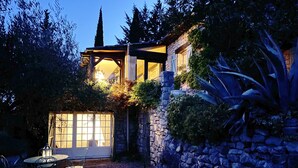 A stone building with a covered patio area, a table with chairs, and a lantern. - Beautiful stone house in olive grove, great pool area and garden, panoramic view (Callas)