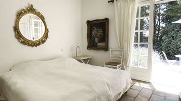 Une chambre à coucher avec un lit, une table de chevet, une chaise, un miroir et une fenêtre avec des rideaux.