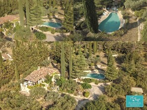 An aerial view of a property with multiple swimming pools, a central building, and surrounding greenery.