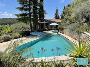 Una piscina con sillas de descanso, rodeada de muros de piedra y abundante vegetación.