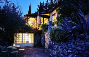 A stone building with a covered patio area, a table with chairs, and a lantern. - Beautiful stone house in olive grove, great pool area and garden, panoramic view (Callas)
