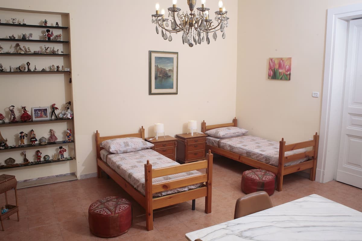 A bedroom with two wooden beds, a chandelier, a shelf with figurines, and a painting on the wall.