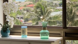 A view from a window overlooking a coastal area with palm trees and houses, a blue vase, and a white orchid on a desk. - Breathtaking Ocean Views! Peaceful Retreat/No Resort Fees. 
 (Honolulu)