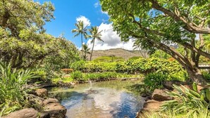 A clear pond surrounded by rocks and lush greenery, with palm trees and a mountain in the background. - Breathtaking Ocean Views! Peaceful Retreat/No Resort Fees. 
 (Honolulu)