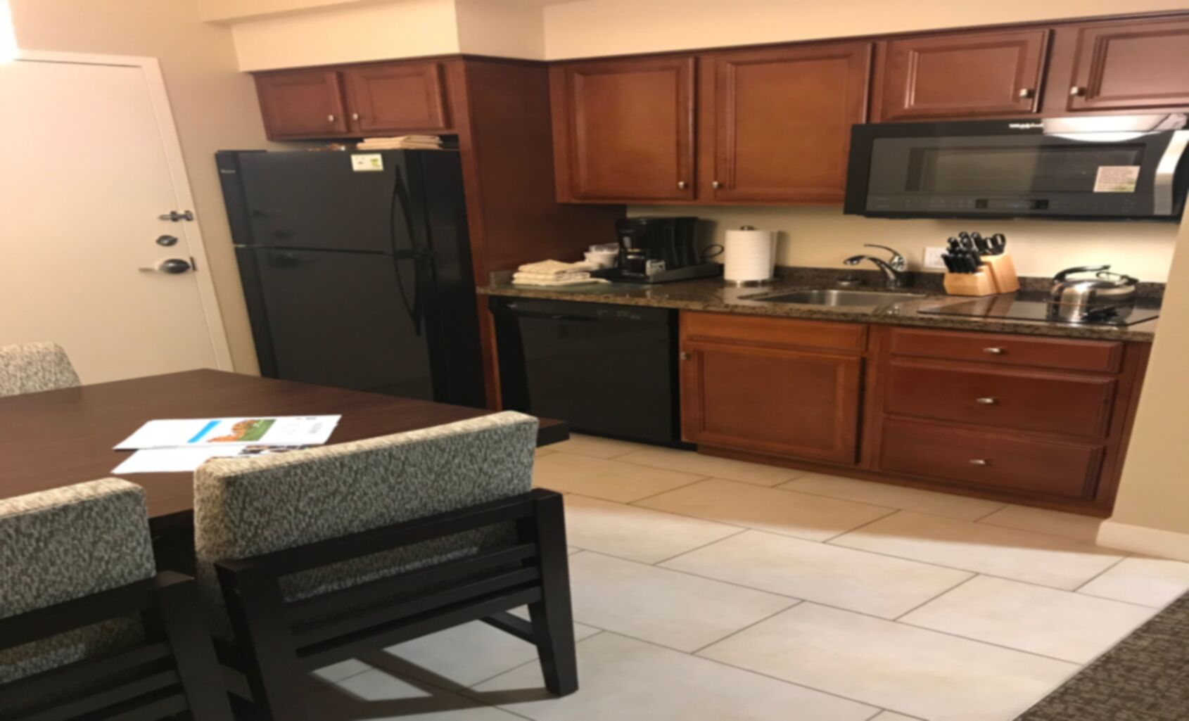 A compact kitchen with wooden cabinets, a black refrigerator, a microwave, and a coffee maker.