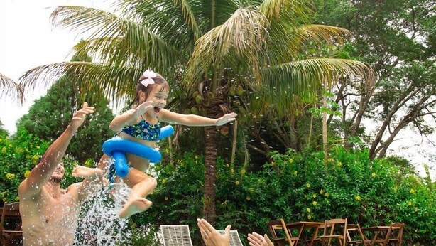 Una piscina con persone che si godono l'acqua, circondata da rigogliosa vegetazione e palme.