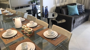 A modern dining area with a glass table set for four, surrounded by wicker chairs. A sofa with cushions is visible in the background. - Landscape Beira Mar, Lindo, Luxo, Vista mar (Fortaleza)