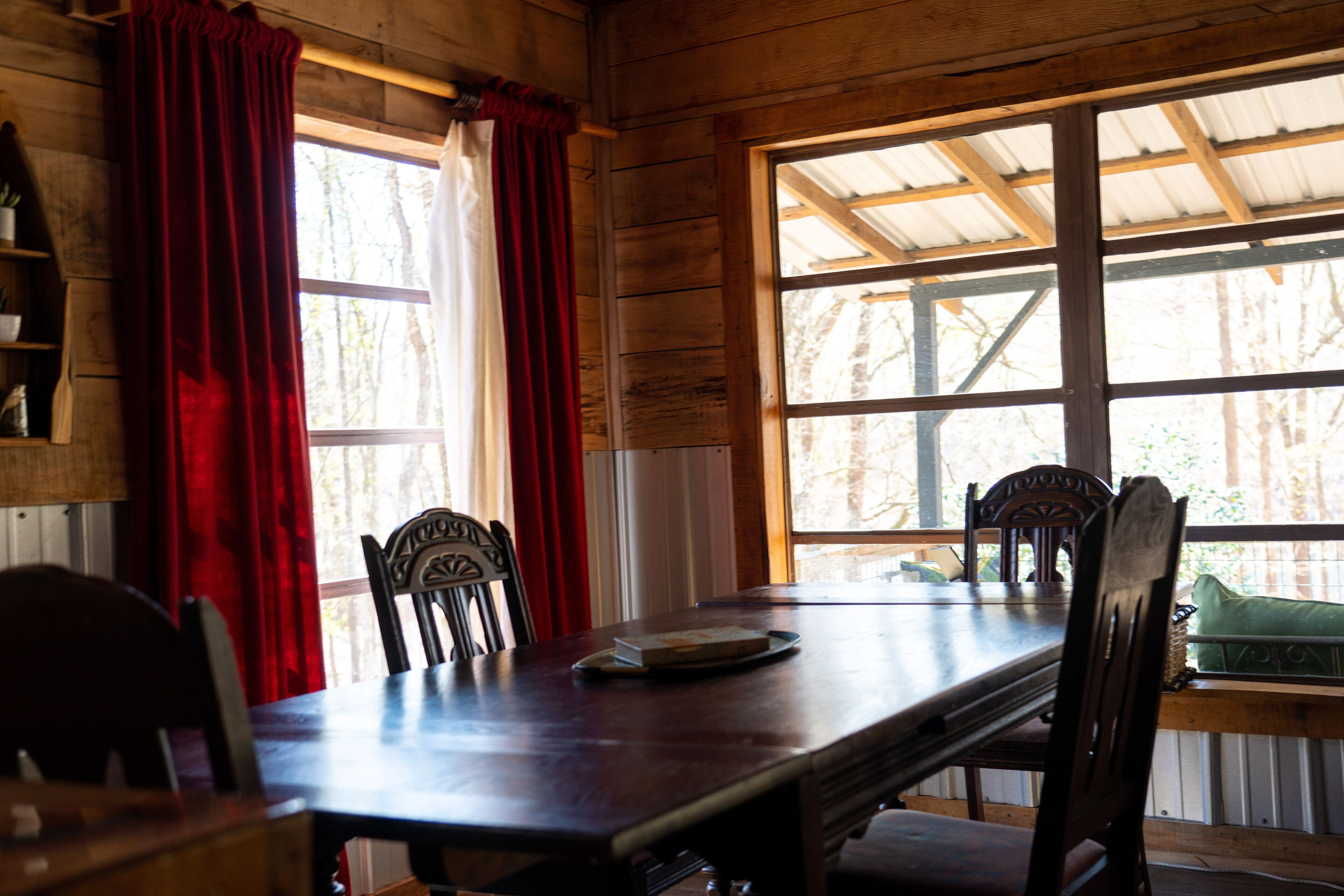 Un interior de madera con una mesa de comedor, sillas y una ventana que da a vistas de árboles.
