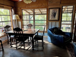 A wooden interior with a dining table, chairs, a blue sofa, and large windows offering a view of trees.