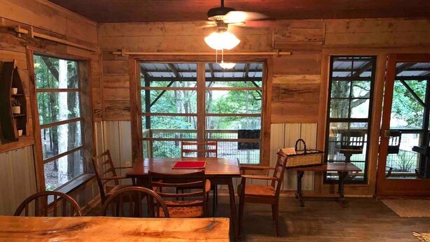 A rustic wooden interior with a dining table and chairs, large windows, and a ceiling fan. - Bowman's Landing Spring House on the Santa Fe River (Fort White)
