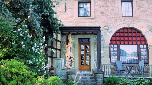 Un bâtiment en pierre avec une porte en bois, un auvent rouge et un balcon avec des chaises.