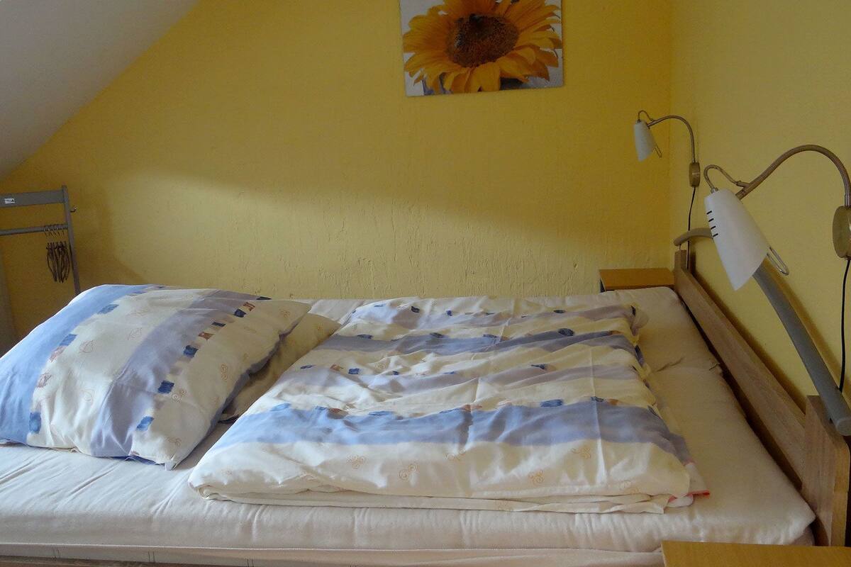 A single bed with a patterned duvet and pillows, a bedside lamp, and a wall-mounted light fixture.