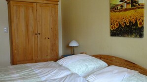 Une chambre avec une armoire en bois, un lit avec une literie blanche et un tableau représentant des tournesols accroché au mur.