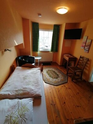 A small room with a bed, a chair, a table, a television, and a window with curtains. - Gästehaus Burg Molbach (Kreuzau)