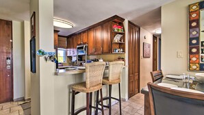 A kitchen with wooden cabinets, a built-in oven, and a dining area with a table and two bar stools. - Loiza Condo w/ Rooftop Patio - Walk to Beach! (Loiza)