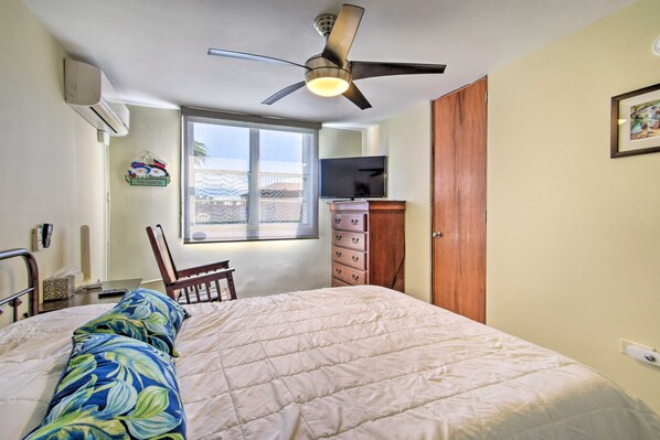 A bedroom with a bed, a ceiling fan, a window, a TV, a dresser, and a chair.