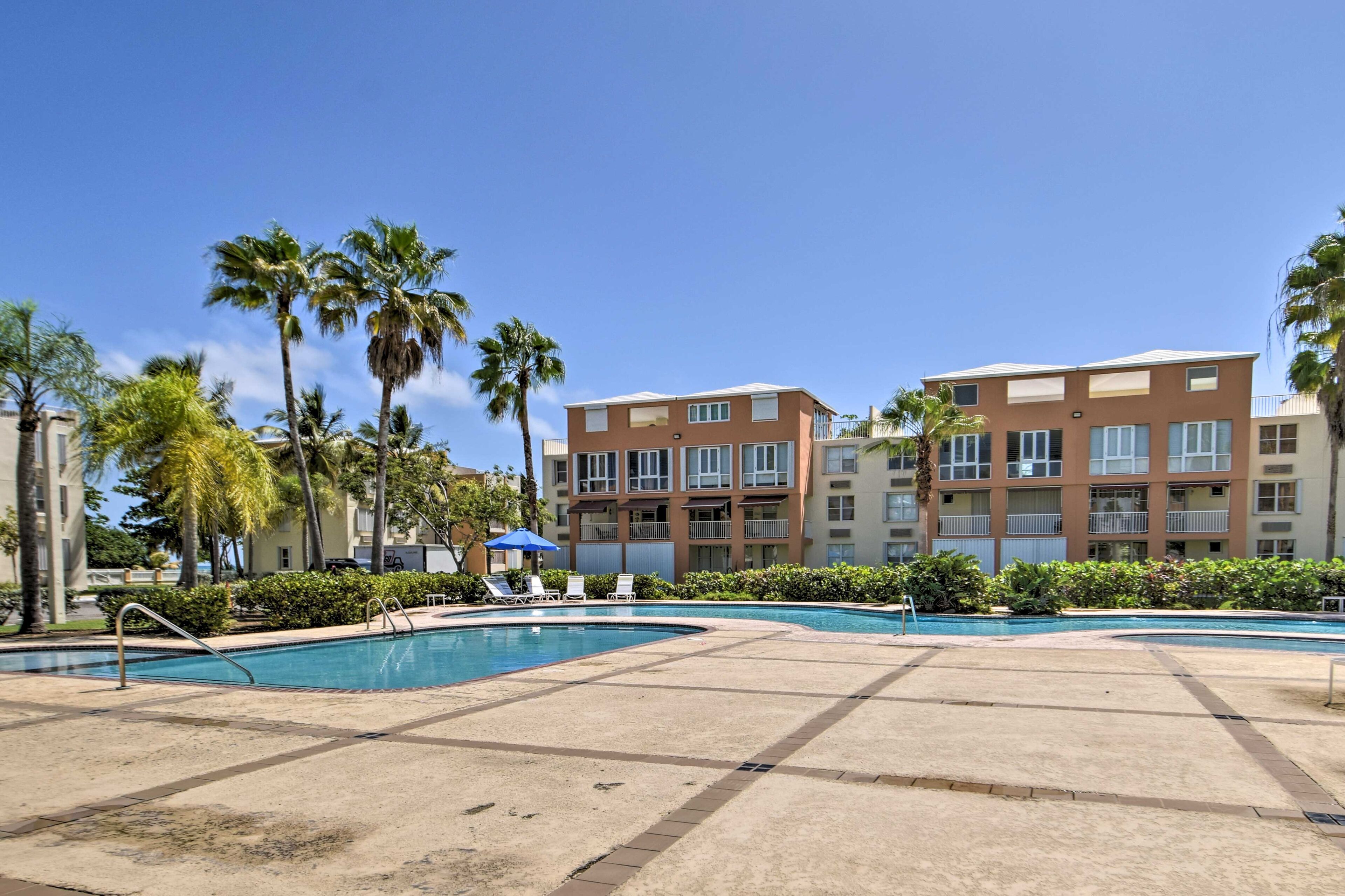 A pool area with lounge chairs and palm trees, surrounded by multi-story buildings.