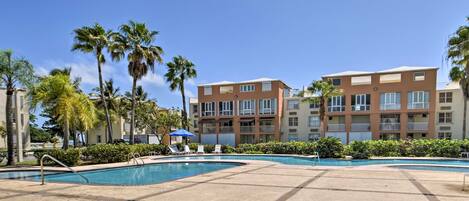 A pool area with lounge chairs and palm trees, surrounded by multi-story buildings.