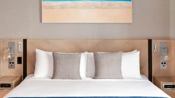 Una cama bien hecha con almohadas blancas y estampadas, una manta azul y un cuadro con motivos playeros.