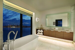 Un baño moderno con una bañera grande, un tocador con espejo y vistas a un paisaje urbano nocturno.