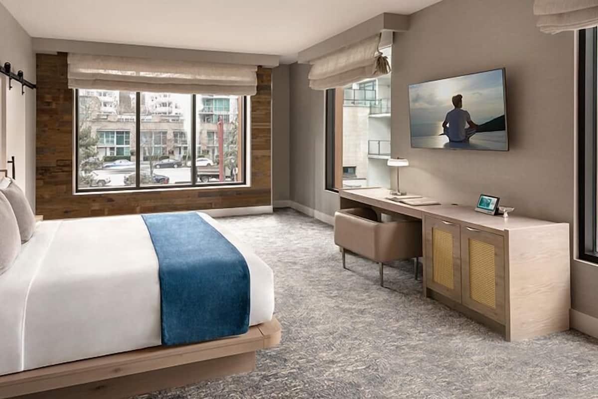 Moderni hotellihuone, jossa on suuri sänky, työpöytä ja näkymä kaupungin ylle.