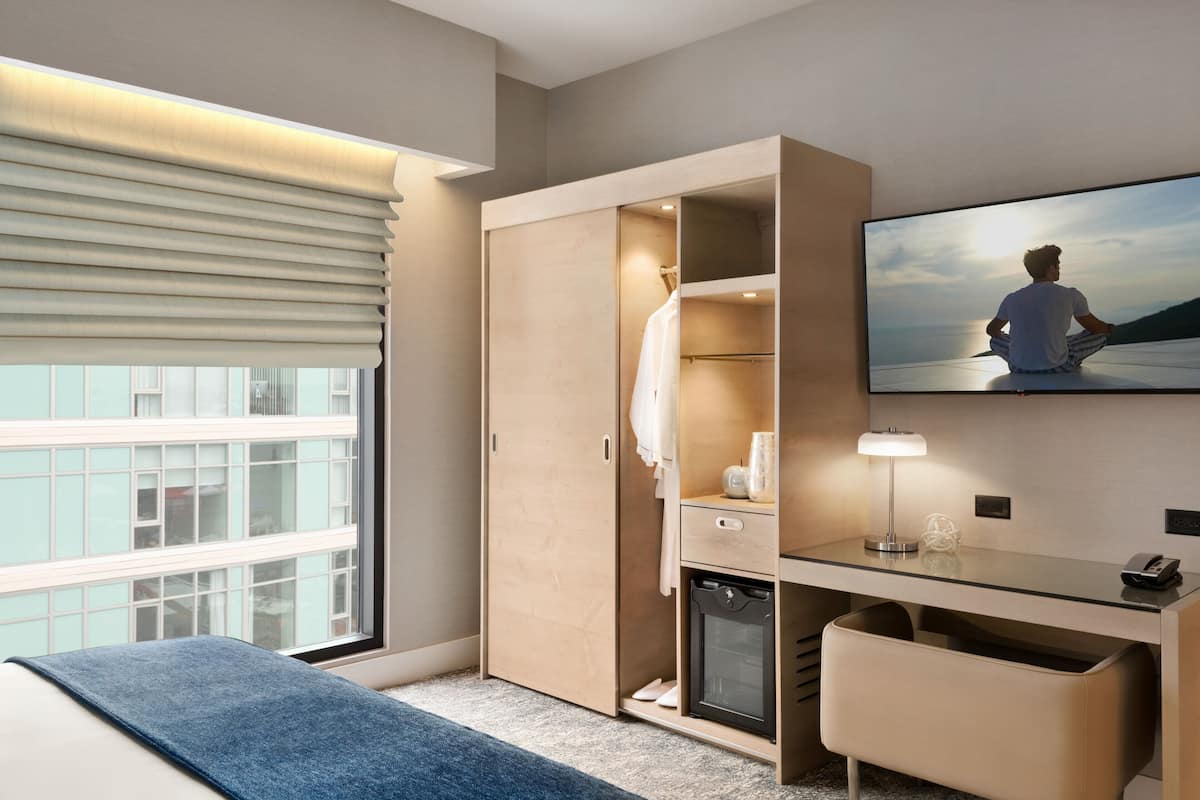 Moderni hotellihuone, jossa on suuri sänky, työpöytä lampun kanssa, vaatekaappi ja televisio, josta näkyy kaunis maisema.