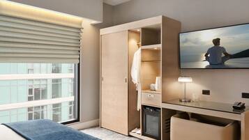 A modern hotel room with a large bed, a desk with a lamp, a wardrobe, and a TV displaying a scenic view.