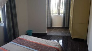 A bedroom with a bed, a wardrobe, a window with curtains, and a tiled floor. - Lapiroguevilla (Grand-Baie)