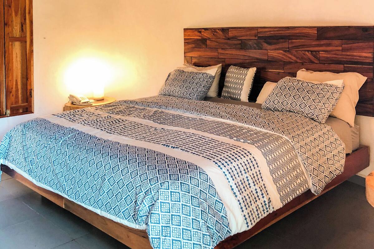 A bedroom with a wooden headboard, a patterned bedspread, and a thatched roof ceiling.