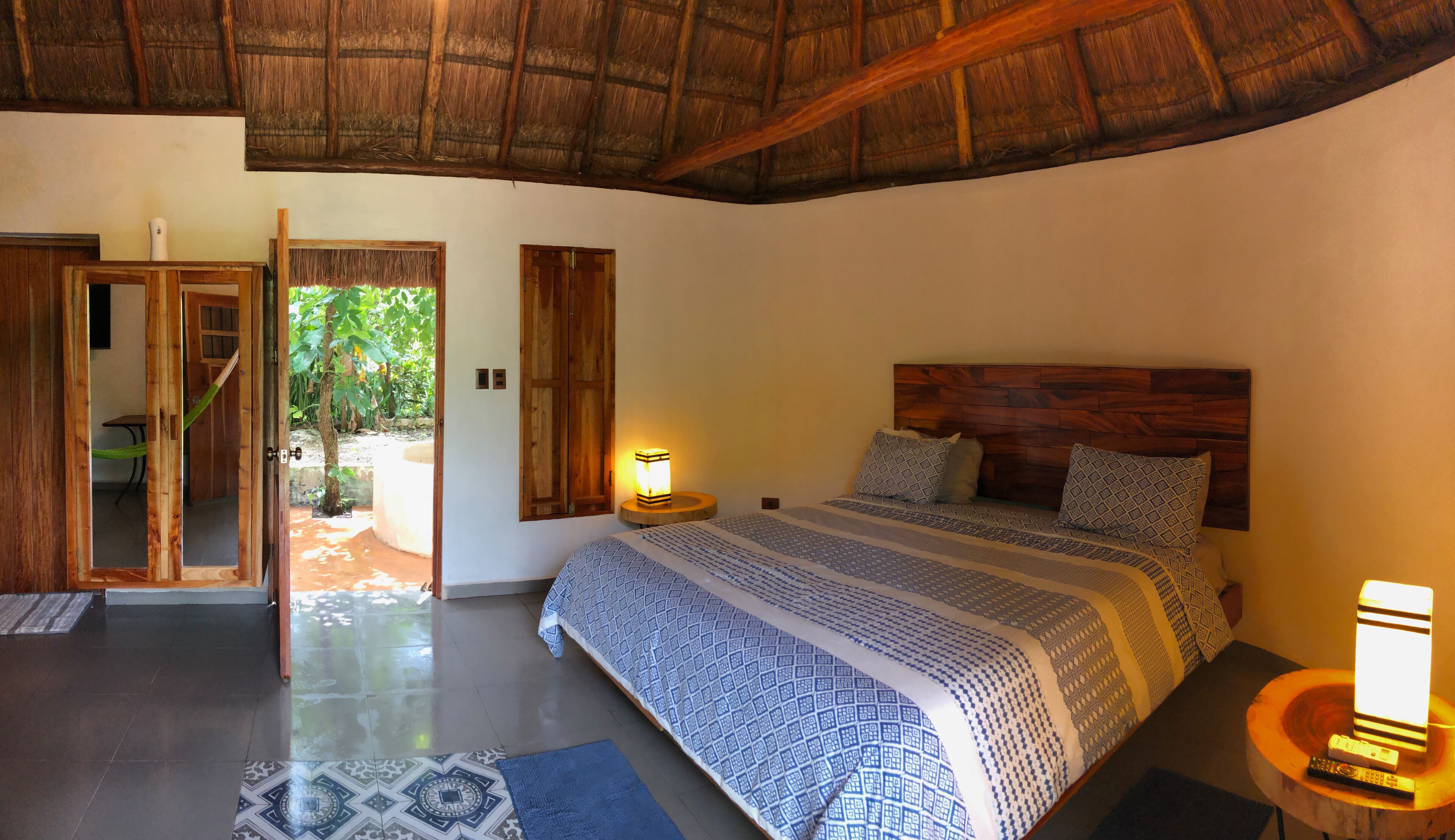 A bedroom with a bed, a nightstand, a lamp, and a door leading to an outdoor area.