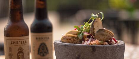 Two bottles of beer and a stone bowl with clams on a tiled table.