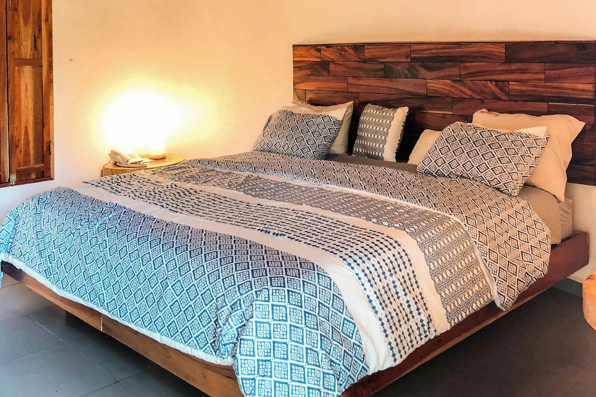 Ein Schlafzimmer mit einem hölzernen Kopfteil, einer gemusterten Bettdecke und einer mit Stroh gedeckten Decke.