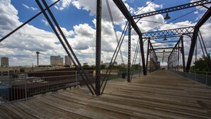 A wooden pedestrian bridge with metal trusses and a view of the cityscape in the background. - Downtown Historic Neighborhood, great location. (San Antonio)