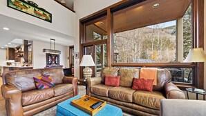 Ein großzügiges Wohnzimmer mit Ledersofas, einem Couchtisch und großen Fenstern mit Blick ins Freie.