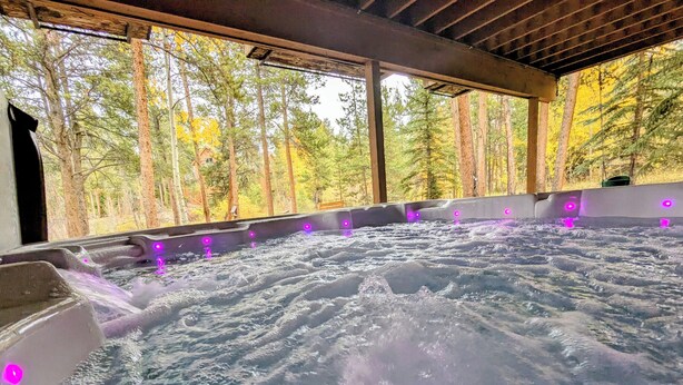 A hot tub with water jets, surrounded by a wooden deck and a forest view. - Riverside Home w/Private Hot Tub, Fire Pit & Deck! (Keystone)