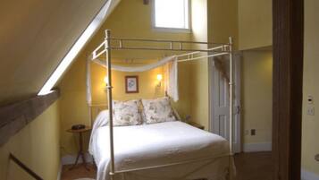 Una cama individual con dosel en una habitación con paredes amarillas, una ventana pequeña y una puerta.
