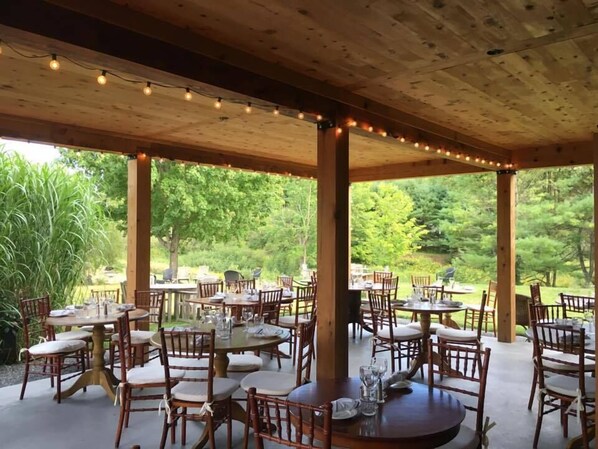 An outdoor patio with wooden tables and chairs, surrounded by greenery. - Gedney Farm (Great Barrington)